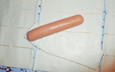 Рецепт - Простой рецепт сосиски в слоеном тесте - Шаг 3 -  Обверни сосиски в два оборота каждым кусочком. Расположи тесто по диагонали, подложи край кусочка теста под сосиску и начинай оборачивать, придерживая хвостик.