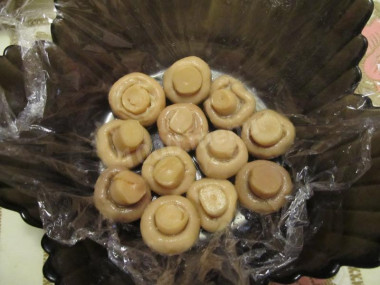 Рецепт - салат грибное лукошко с шампиньонами и солеными огурцами - Шаг 3 -  Дно и края высокого блюда, в котором планируется подавать салат,  застилаем пищевой пленкой. При желании можно на дно насыпать измельченный укроп. Первым слоем выкладываем шампиньоны шляпками вниз.